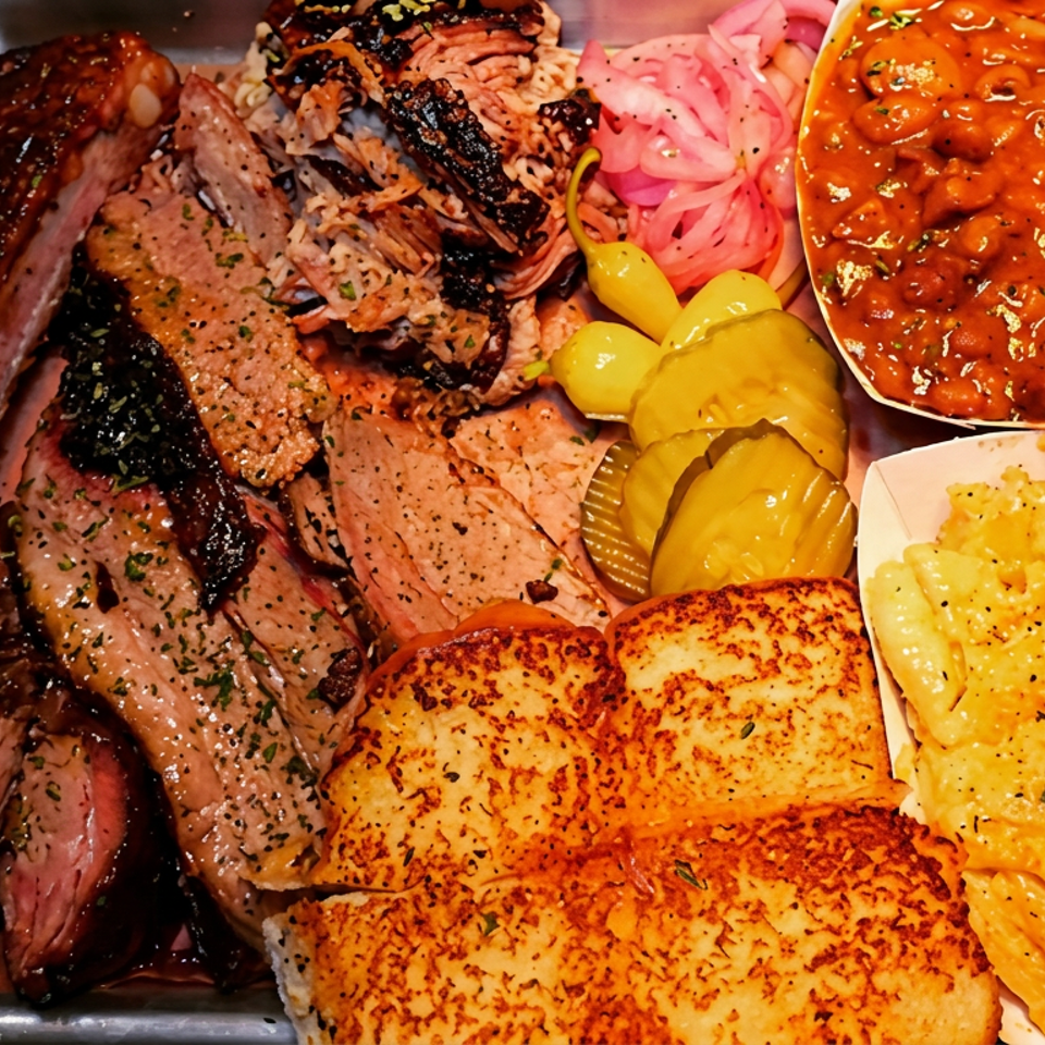 Barbecue platter with ribs, sliced smoked meats, baked beans, macaroni and cheese, pickles, onions, and toasted bread.