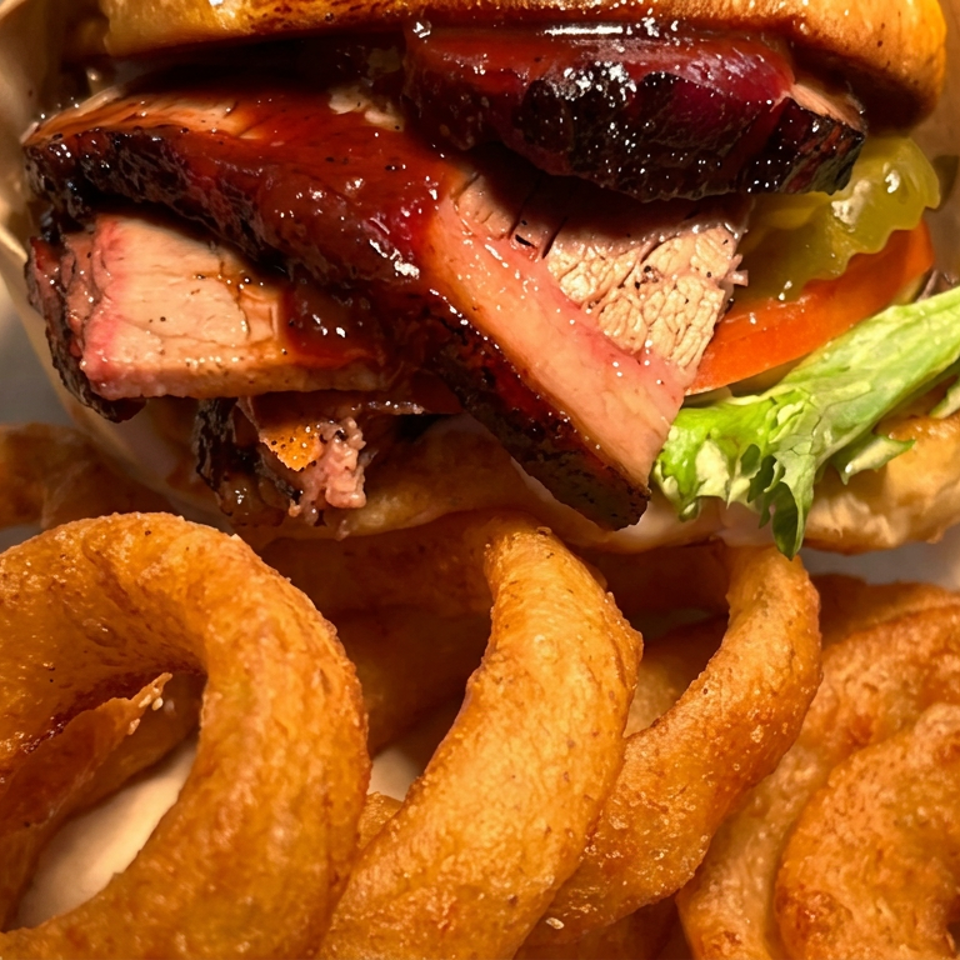 Stacked roast beef sandwich with lettuce and tomato served alongside golden onion rings in a paper-lined basket.